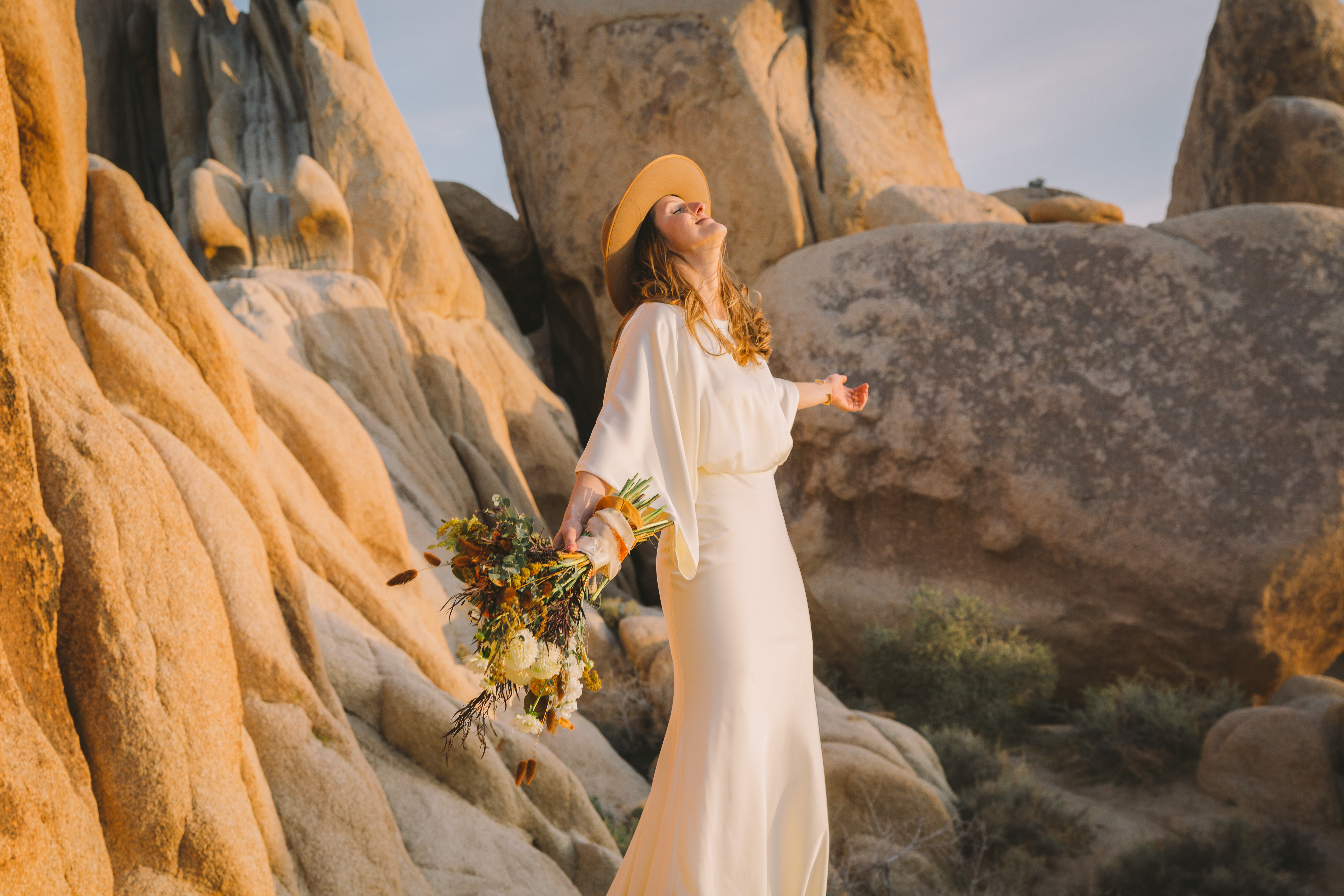 girl in wedding dress leans back and enjoys the desert sun in joshua tree national park on her elopement day
