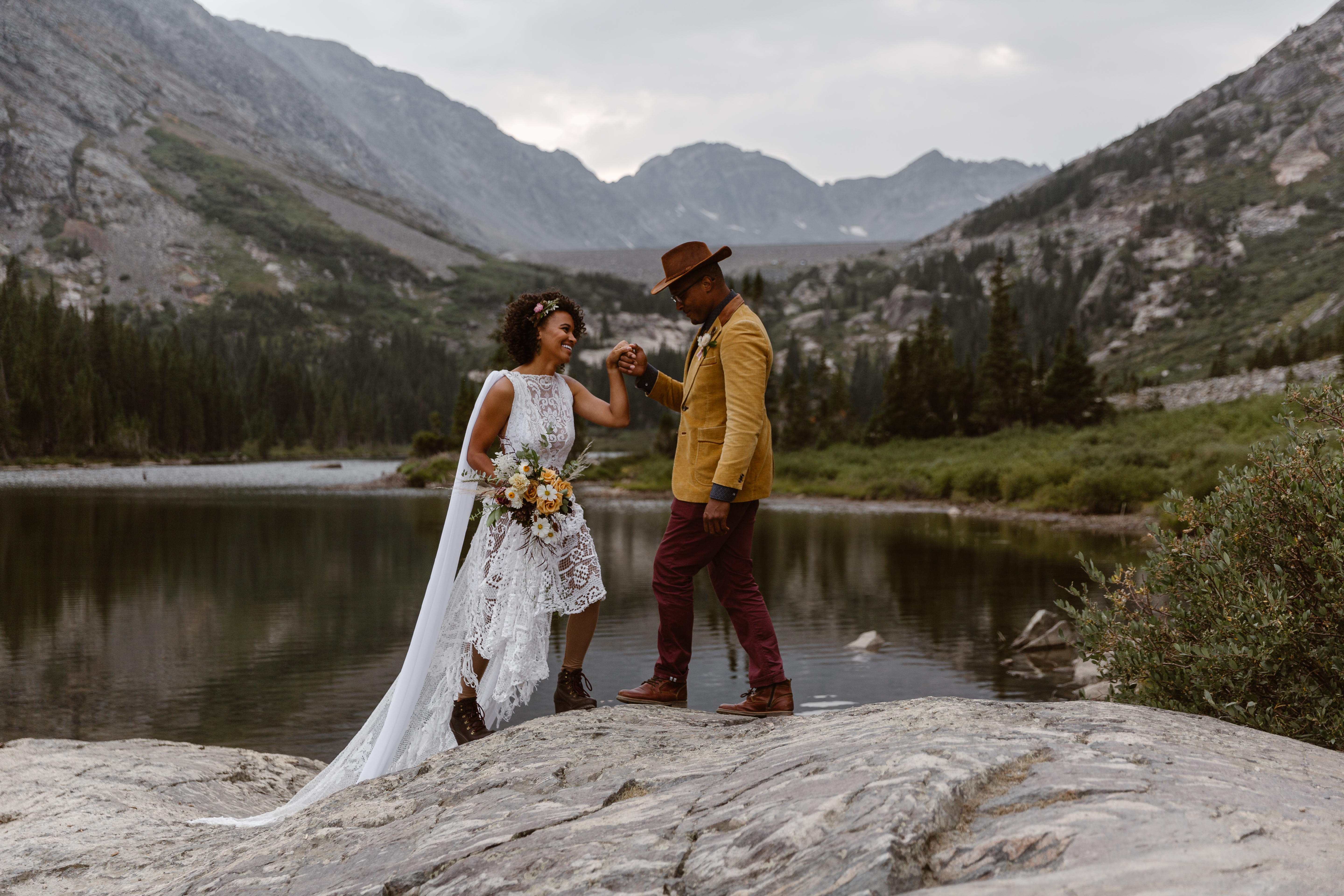 Eloping Couple climbs up a rock in Colorado by a lake