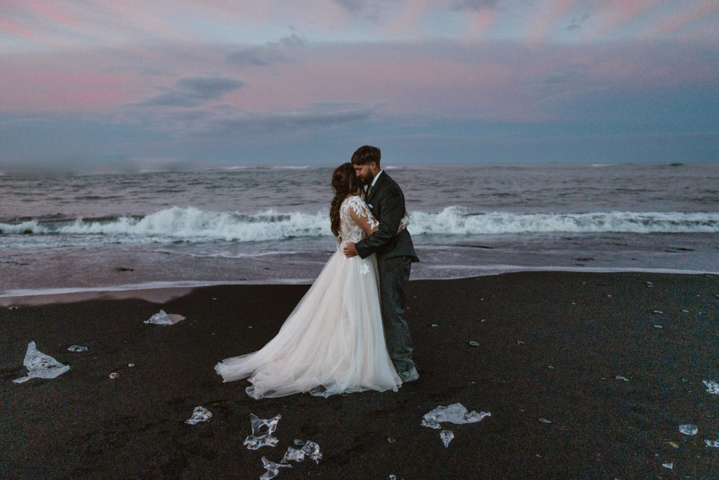 A couple kisses on an Iceland beach during sunset during their Iceland elopement