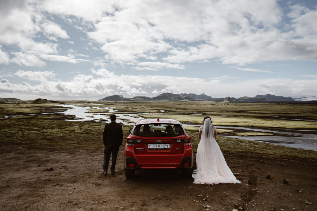 A bride and groom stand beside their car during their Iceland elopement