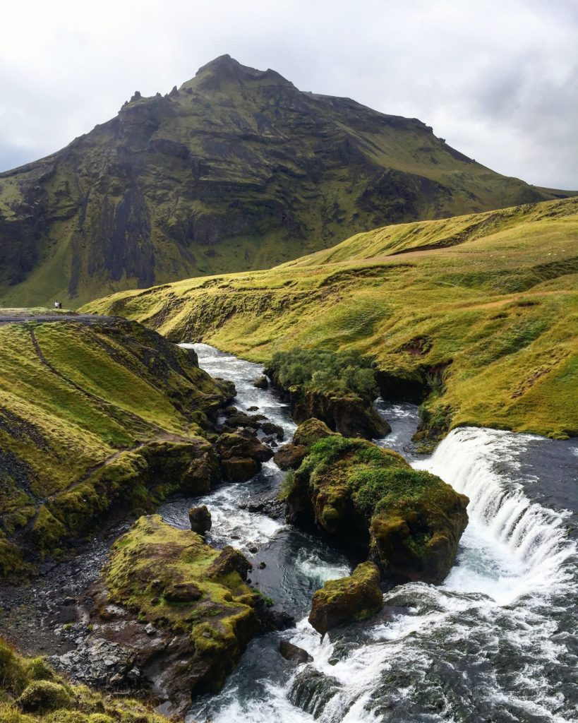 green rolling hills of iceland with a mountain peak in the background