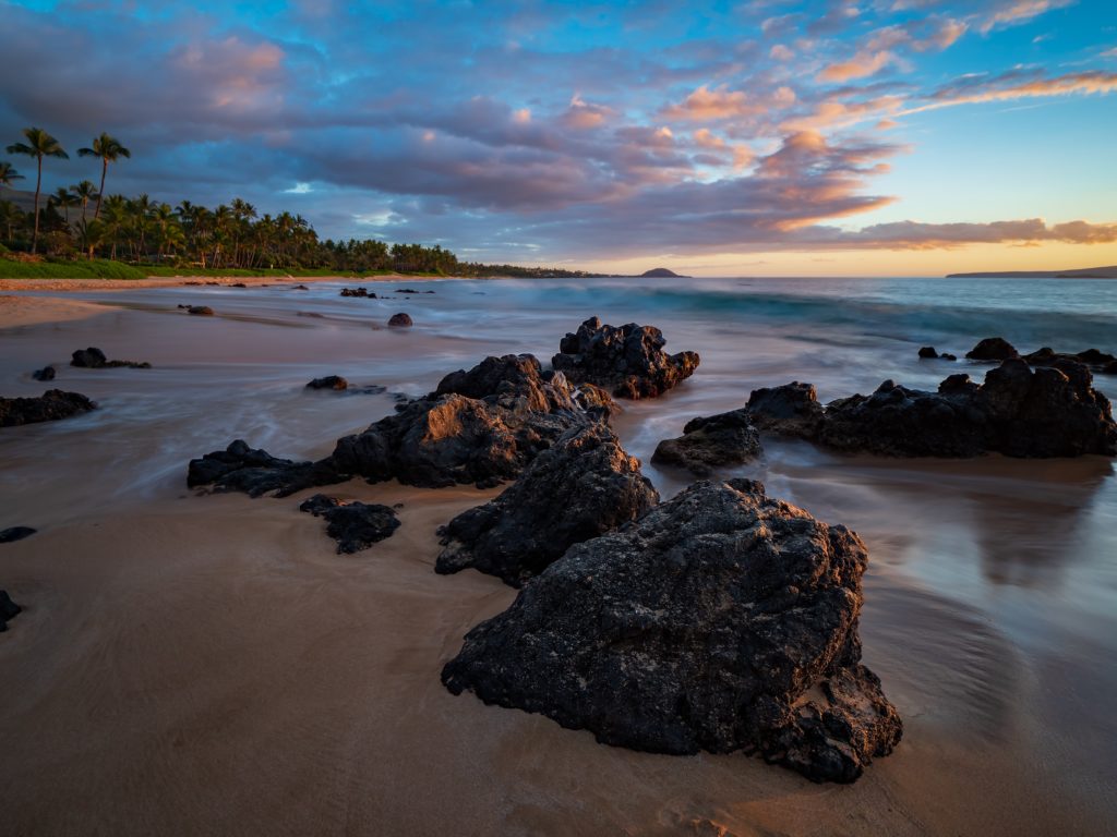rocks on a hawaii beach as the sun sets with purples and pinks in the sky