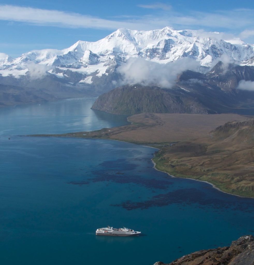An aerial view of South Georgia Island with snow capped mountains and rolling fields of green
