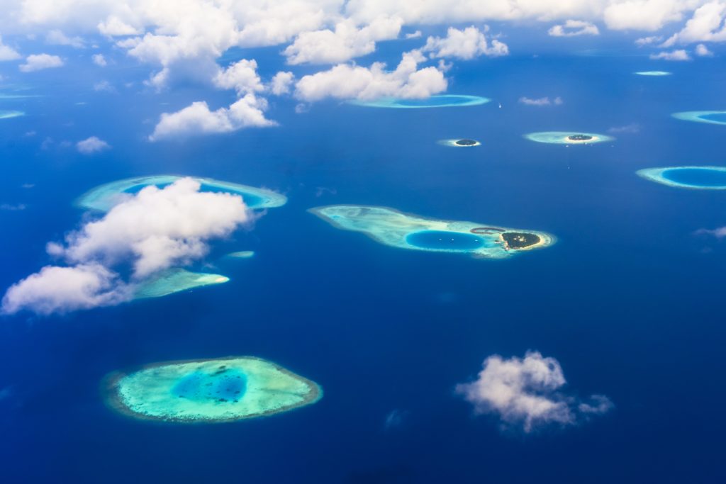 Patches of light blue water surrounding islands in the middle of darker blue water in the Maldives