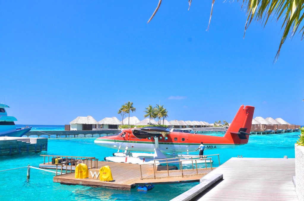 A red and white seaplane lands on a small dock in the Maldives
