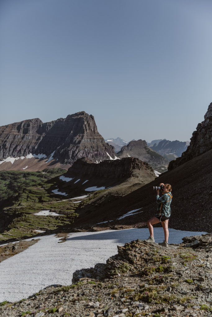 A photographer stands on the edge of a hill as she photographs the mountains in the background