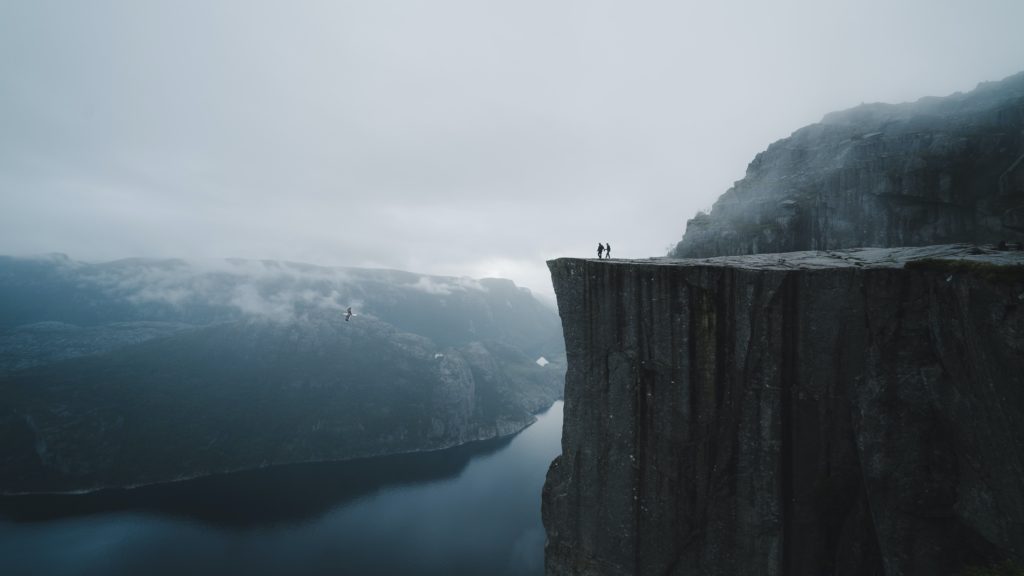 A person stands on a cliff overlooking a sprawling lake in Norway
