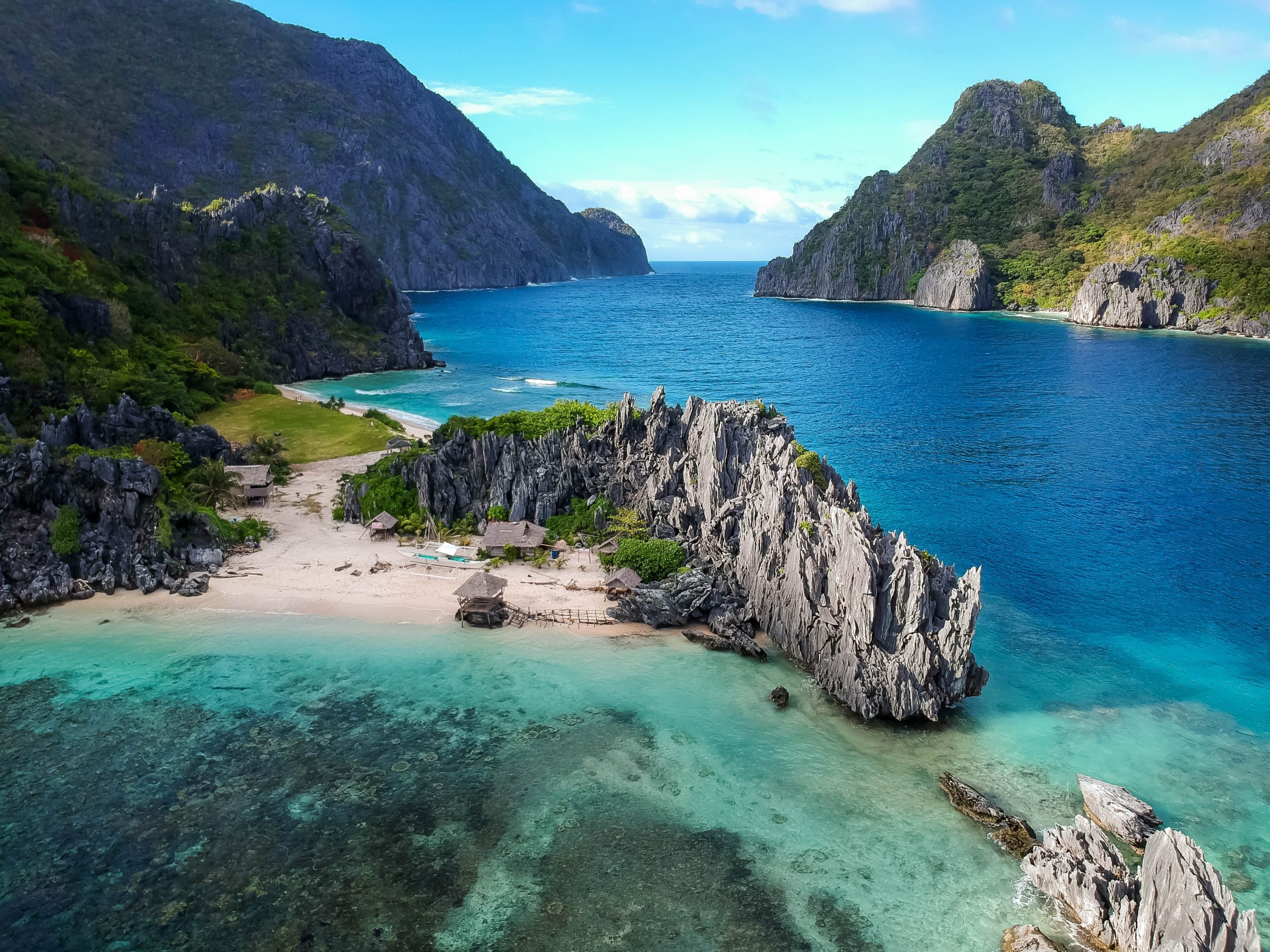 A rocky features on the beach surrounded by clear water and mountans in the Philippines