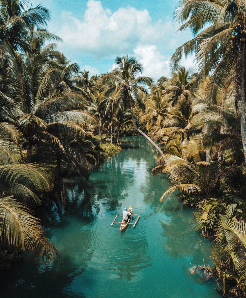 A boat floats down a turquoise river surrounded by palm trees