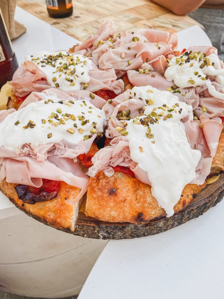 Pieces of focaccia are covered with sliced ham, burrata, and pistachios. 