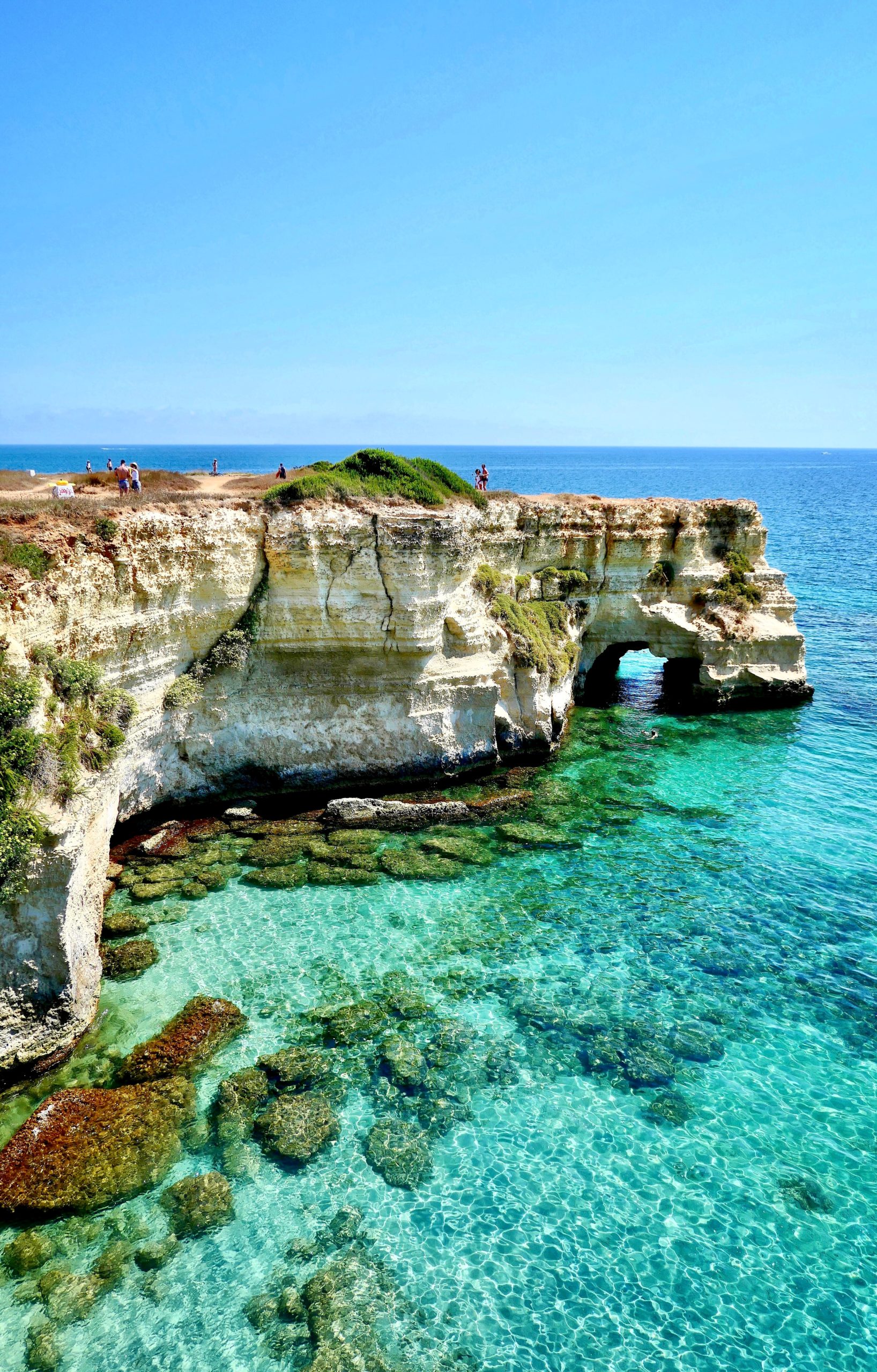 A rocky cliff towers over crystal clear ocean water in Puglia, Italy