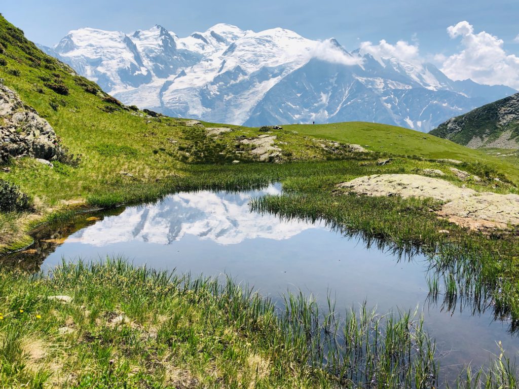 A lake relfects the snow-covered mountains in the distance in the summer in the French Alps