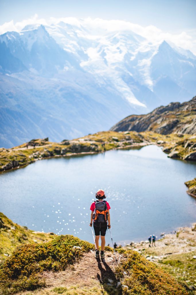 A hiker stands above a lake in the summer in the French Alps