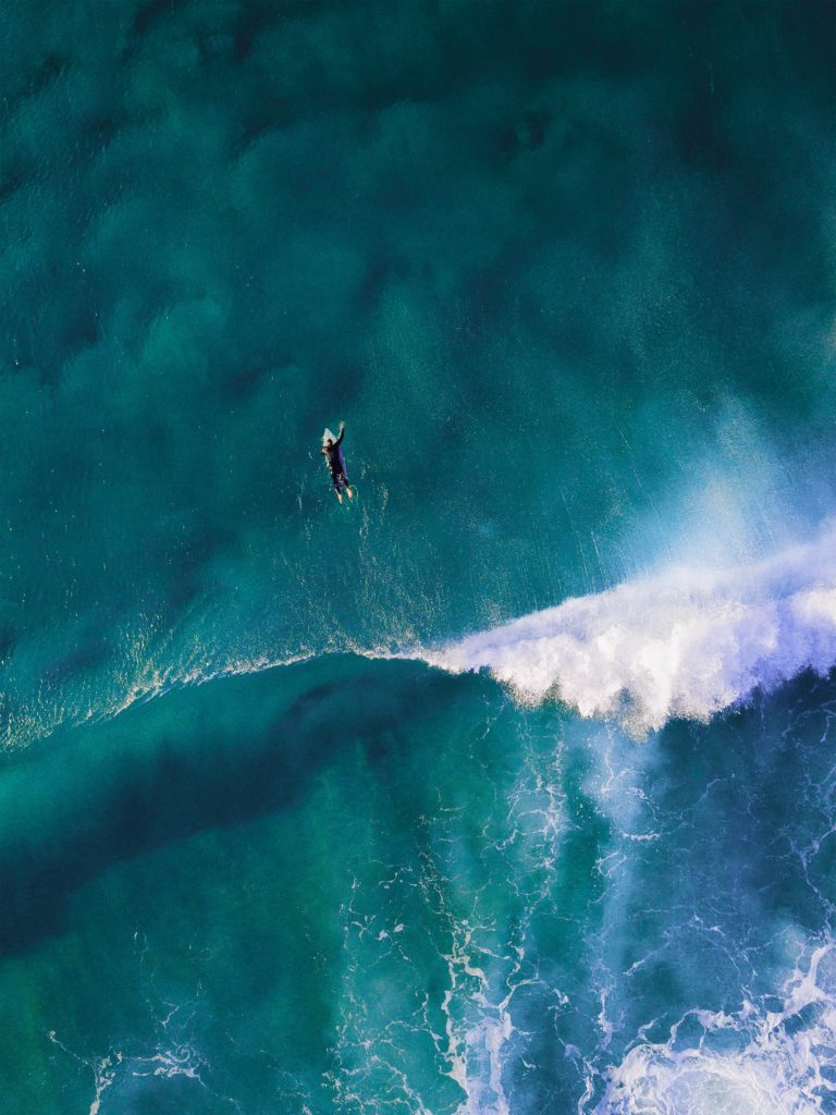 A surfer swims on his board past the waves