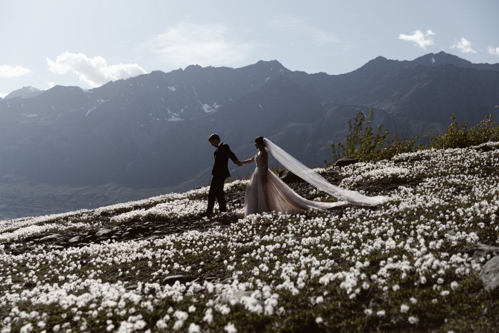 A couple walks through wildflowers in Alaska during their Alaska elopement
